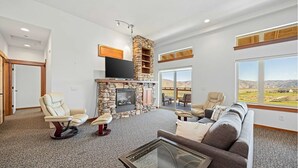 A spacious living room with a stone fireplace, comfortable seating, and large windows offering a view of the landscape. - Desert Canyon Golf Resort (Orondo)