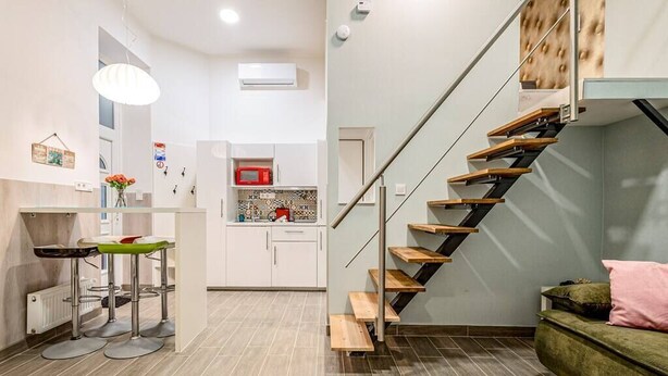 A modern apartment with a kitchen, a dining area with bar stools, a staircase, and a green sofa. - X - Bella Apartment II Budapest (Budapest)