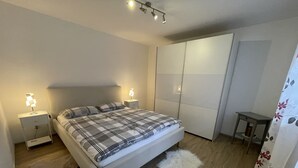 A bedroom with a bed, bedside tables, a wardrobe, a small table, and a fluffy rug. - New comfort apartment. Basement, good for excursions, Europapark, Strasbourg (Ortenberg)