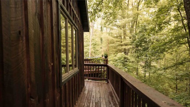 A wooden deck with a view of a dense forest. - Hemlock Haven,Hot-tub,Private,30 min to Penn State (Mill Hall)