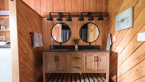 A wooden cabin-style bathroom with a wooden vanity, two round mirrors, and a black pendant light fixture. - Hemlock Haven,Hot-tub,Private,30 min to Penn State (Mill Hall)
