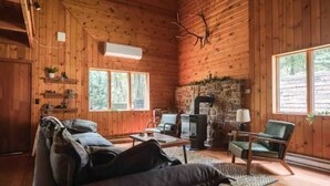 A cozy cabin interior with wooden walls, a stone fireplace, a sofa, and a chair. - Hemlock Haven,Hot-tub,Private,30 min to Penn State (Mill Hall)