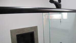 Een badkamer met een glazen douchecabine, een zwarte handdoekhouder en een klein ventilatierooster.
