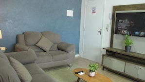 Een woonkamer met een bank, een bijzettafeltje met een plant, en een aan de muur bevestigde televisie.