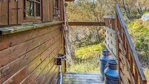 Une cabane en bois avec un escalier en bois menant à une terrasse, entourée d’arbres et d’une zone herbeuse.