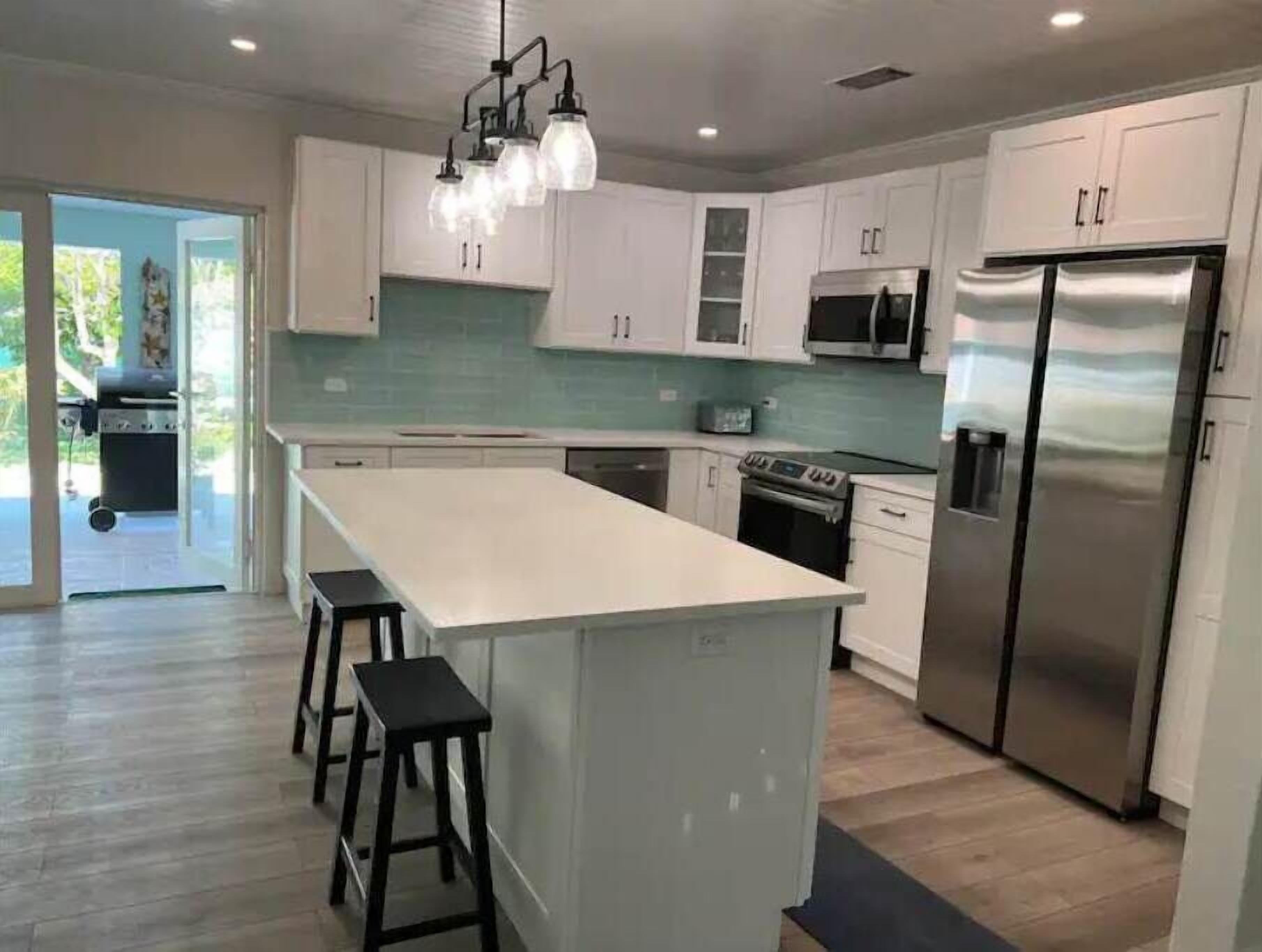 A modern kitchen with white cabinets, a stainless steel refrigerator, and a central island with stools.