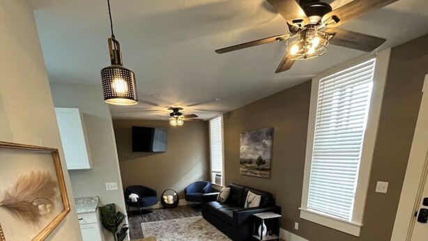 A modern living room with a wooden dining table, a ceiling fan, and a large window with blinds. - Manitou Apartment 2B (Manitou Springs)