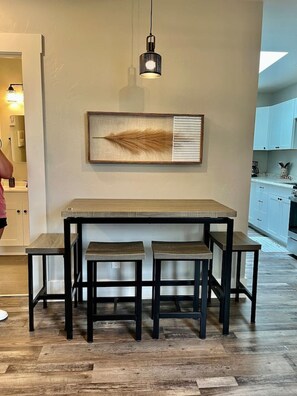 Uma cozinha moderna com uma mesa de madeira e dois banquetes, uma luminária pendente e uma obra de arte emoldurada na parede.