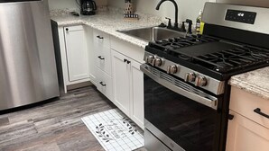A modern kitchen with white cabinets, a stainless steel refrigerator, a gas stove, and a microwave. - Manitou Apartment 2B (Manitou Springs)