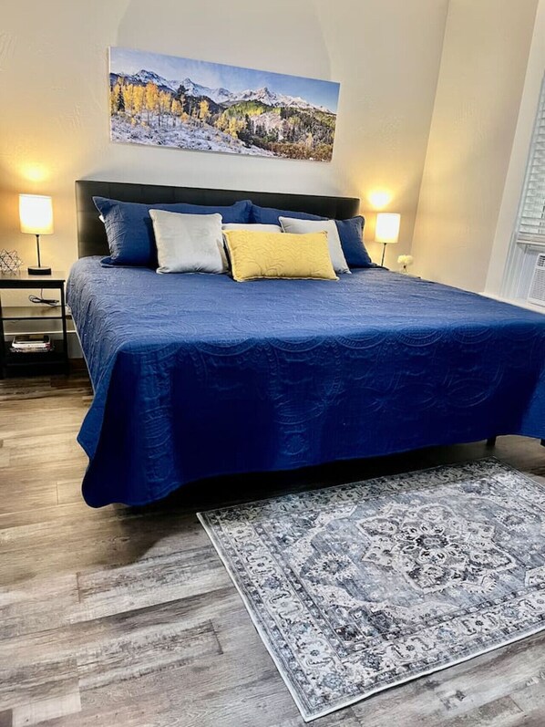 Quarto com uma cama grande, cabeceira, duas mesas de cabeceira com abajures, um tapete e um quadro na parede.