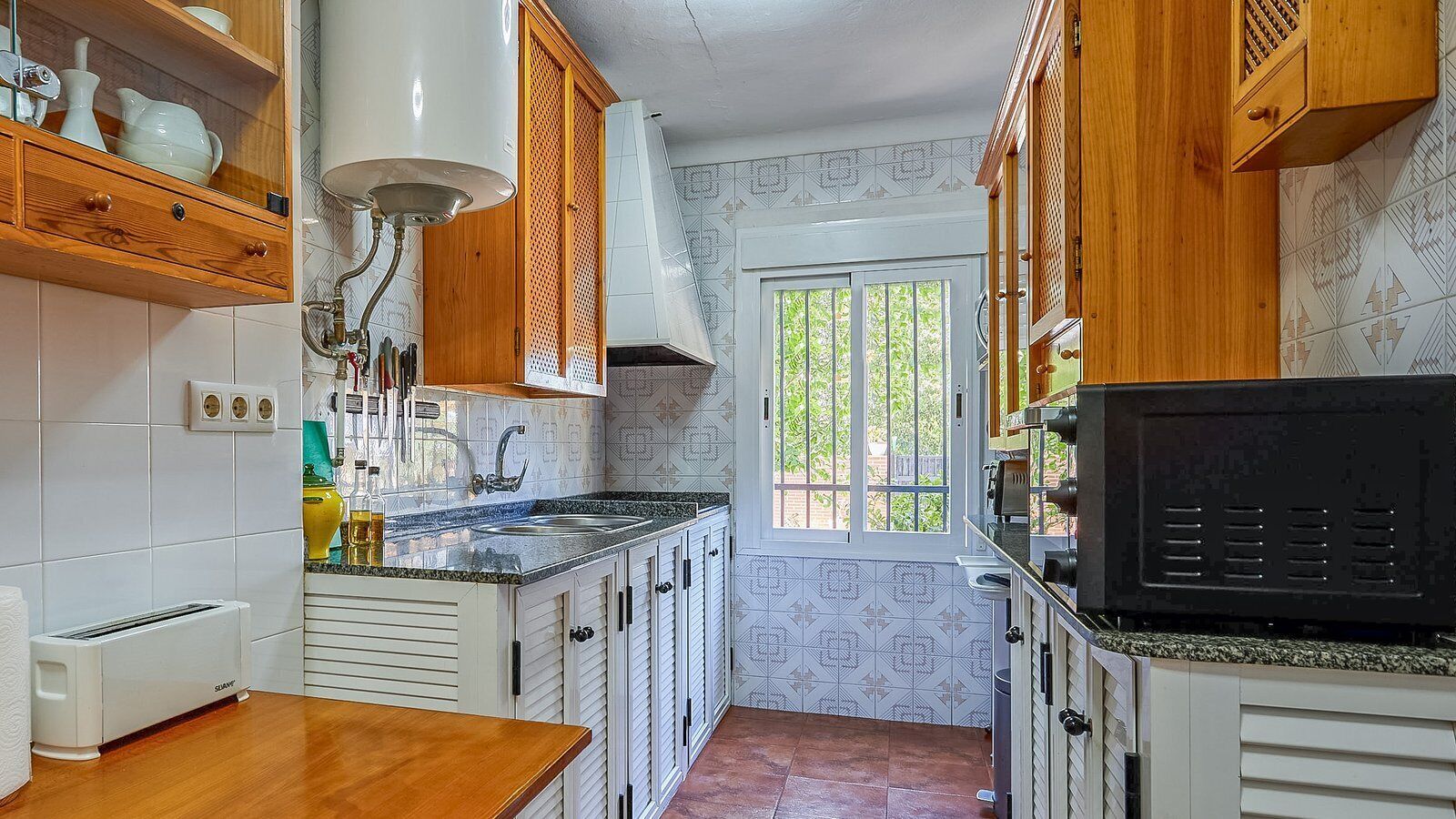 A compact kitchen with white cabinets, a granite countertop, a built-in microwave, and a window providing natural light.