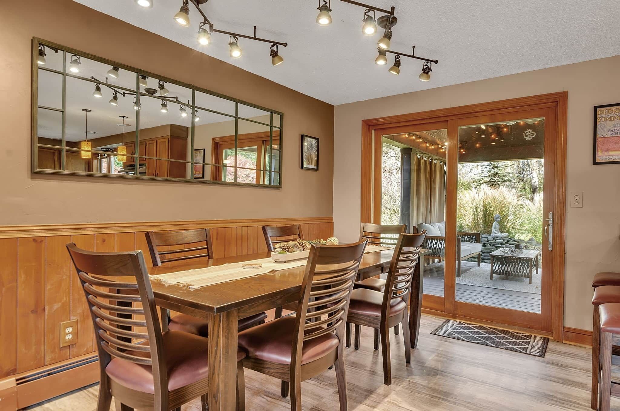 Zona pranzo con tavolo e sedie in legno, un grande specchio e una porta scorrevole in vetro che dà su un patio esterno.