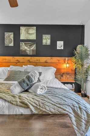 Un lit avec une tête de lit en bois, une couverture et des oreillers. Des œuvres d’art sont accrochées au mur au-dessus du lit.