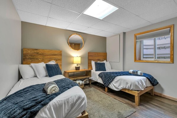 Une chambre d’hôtel avec deux lits, une table de chevet avec une lampe, un miroir et une fenêtre.