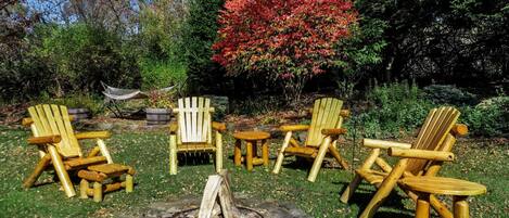 Un hogar de fuego rodeado de sillas Adirondack de madera en un jardín.