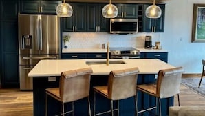 Una cocina moderna con armarios oscuros, electrodomésticos de acero inoxidable y una isla central con taburetes de bar.