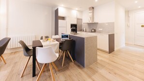 Een moderne keuken met een centraal eiland, een eetgedeelte met vier stoelen en een kleine tafel met ontbijtartikelen.