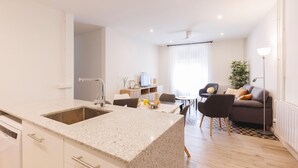 Een moderne keuken met een granieten aanrecht en witte kasten, een eethoek met een tafel en stoelen, en een woonkamer met een bank en een vloerlamp.