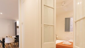 Een moderne hotelkamer met een houten vloer, een bed met een oranje sprei, een witte deur en een klein bureau met een stoel.