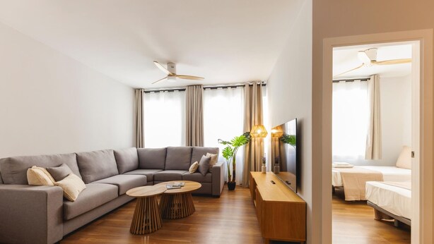 Un salon moderne avec un canapé d’angle gris, des tables basses en bois, un téléviseur et une console en bois.