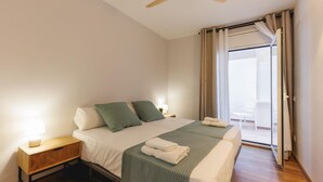 Une chambre à coucher avec un lit, des tables de chevet, un ventilateur de plafond et une vue sur l’extérieur.
