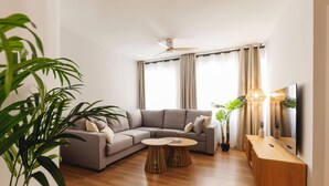 Un salon moderne avec un canapé d’angle gris, une table basse en bois et un téléviseur posé sur un meuble en bois.