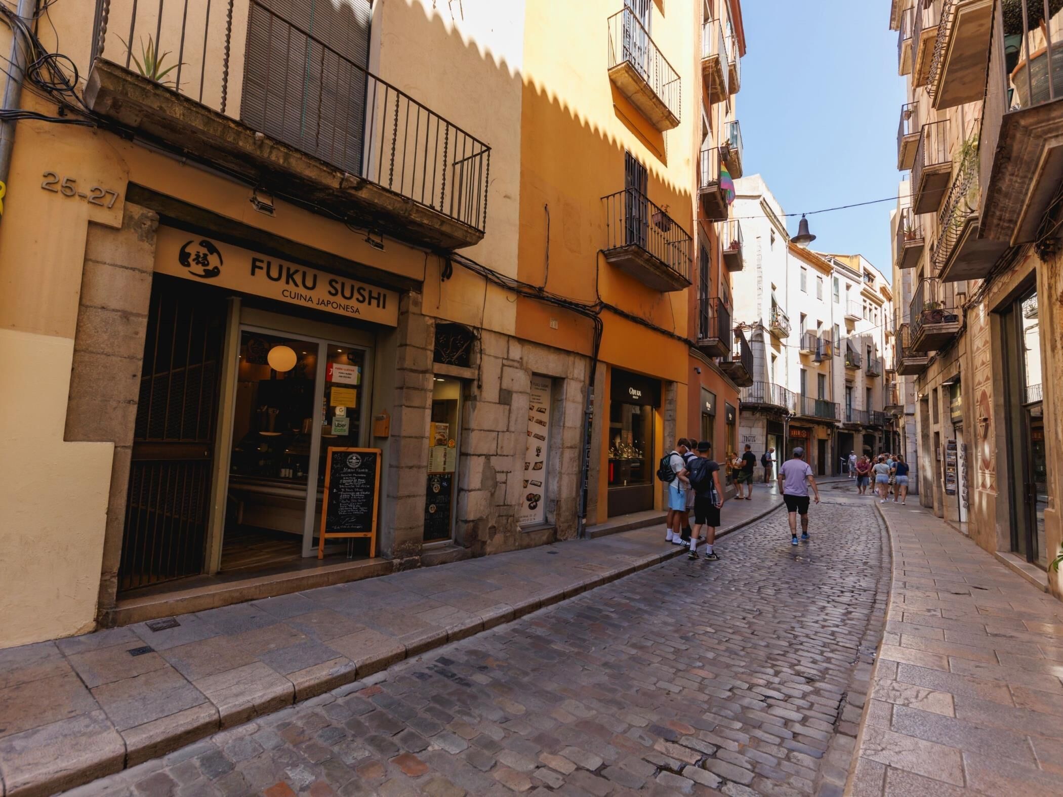 Una calle adoquinada con un restaurante de sushi llamado Fuku Sushi.