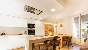 A modern kitchen with white cabinetry, a central island, and a dining area with wicker chairs.