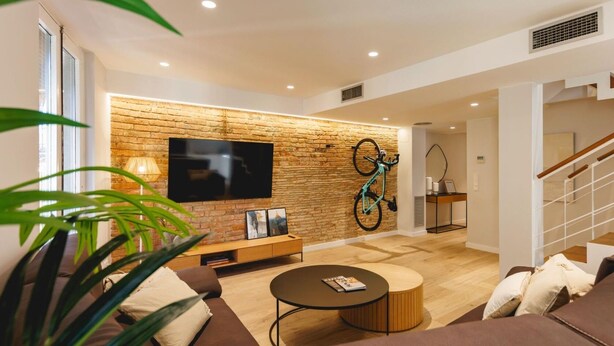 A modern living room with a brick accent wall, a mounted TV, a bicycle, and a staircase leading to another level.
