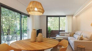 Un salon moderne avec une table à manger ronde en bois, un canapé beige et de grandes fenêtres donnant sur la verdure.