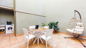 A compact living space with a wooden table, white chairs, a hanging chair, a washing machine, and potted plants. - Bravissimo Plaça Catalunya, apartment with terrace (Girona)