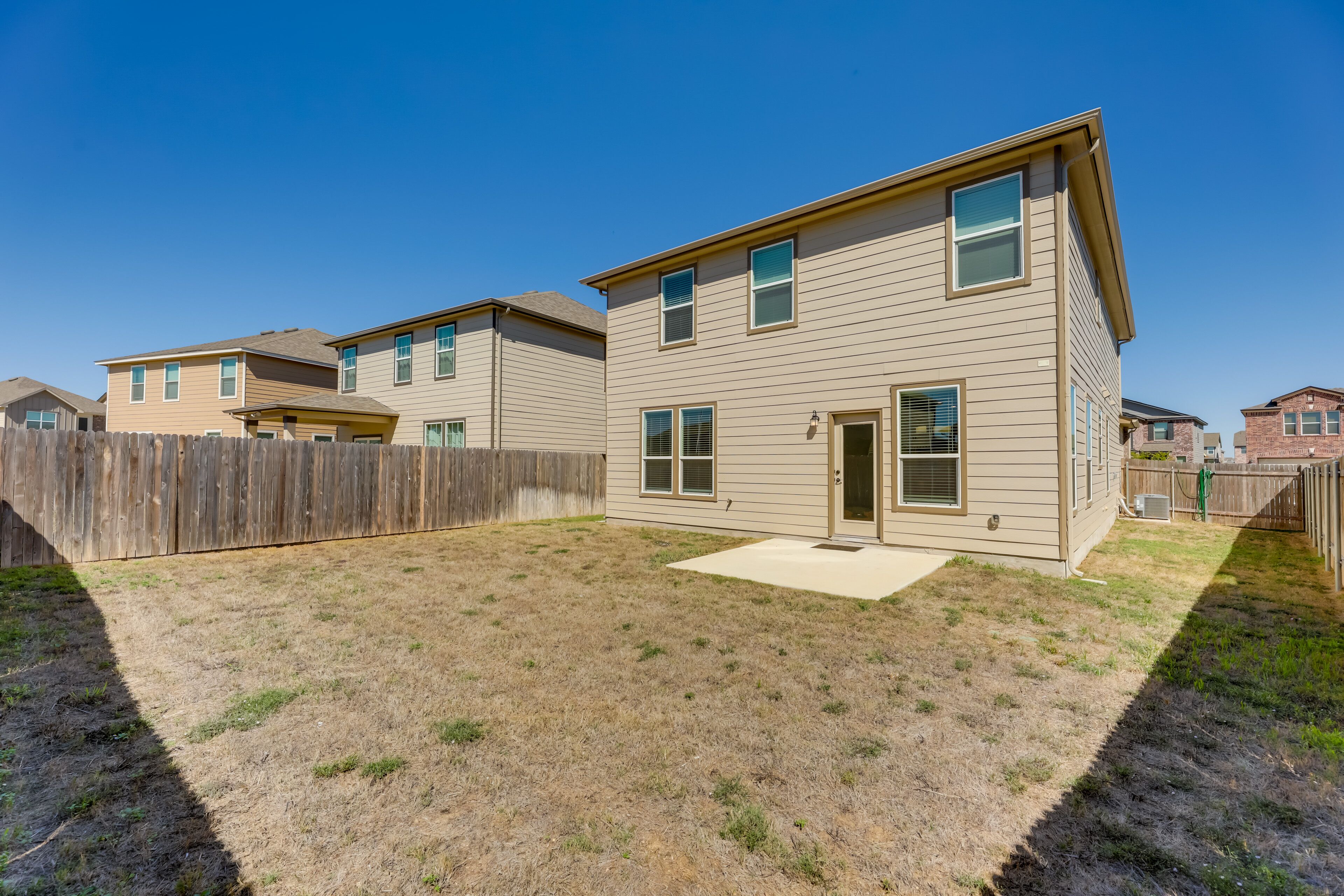 A residential building with a fenced backyard, a small patio, and a wooden fence.