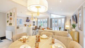 Un comedor moderno con una mesa redonda dispuesta para cuatro personas, una cocina al fondo y un ventanal grande que proporciona luz natural.