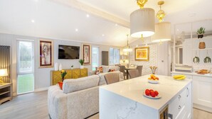 Una cocina moderna con una isla de mármol, un rincón de comedor con sofá y un televisor montado en la pared.