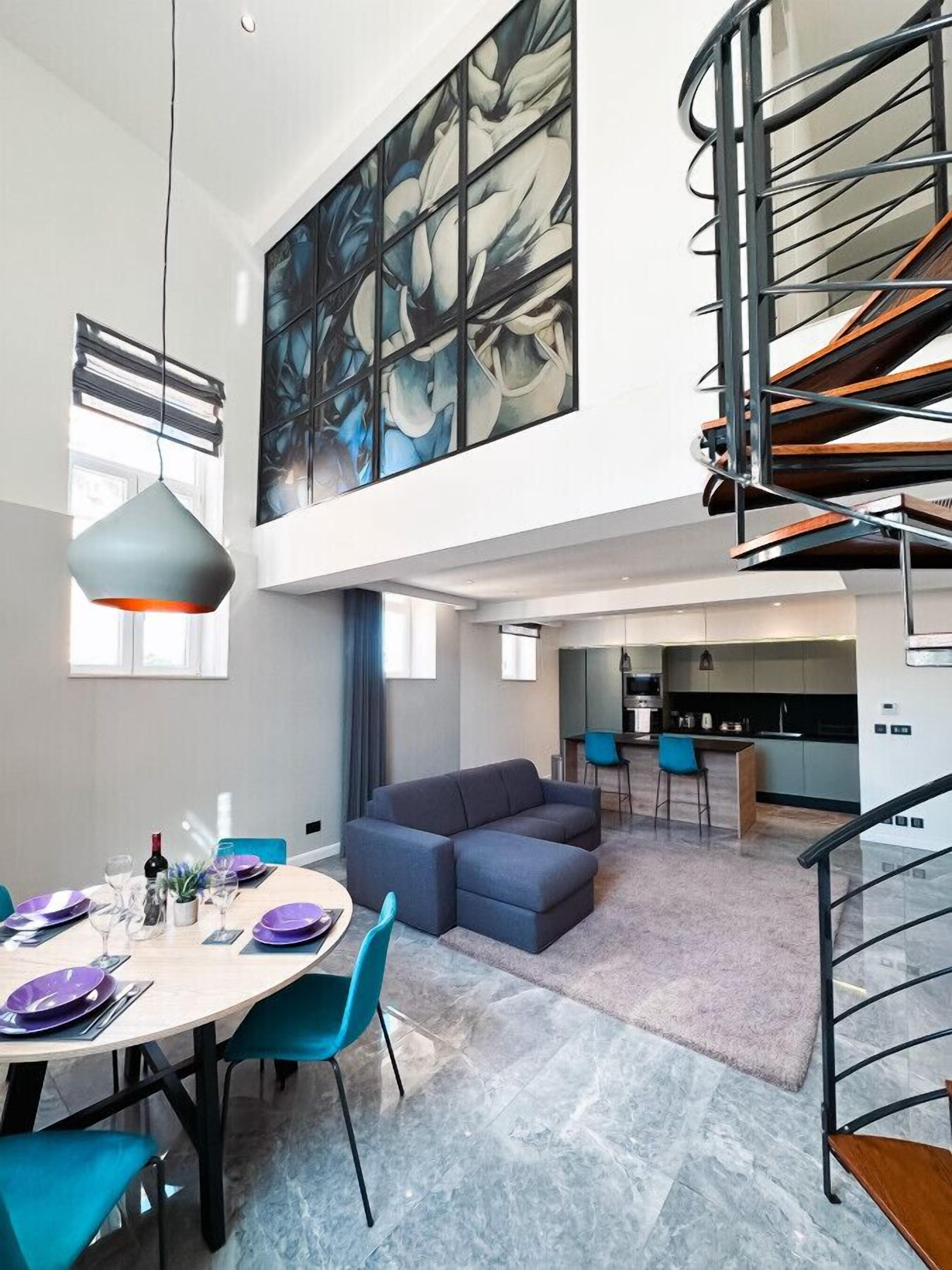 A modern interior with a dining area, a large abstract painting, a staircase, and a kitchen.