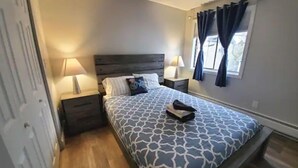 A bedroom with a bed, nightstands, a window with curtains, and a door.
