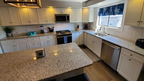 Een moderne keuken met granieten aanrechtbladen, roestvrijstalen apparatuur en witte kasten.