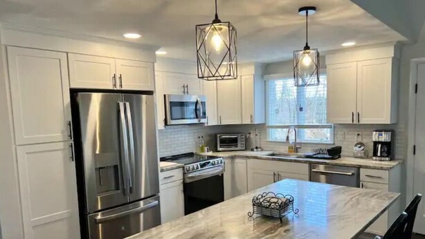 A modern kitchen with white cabinets, stainless steel appliances, and a marble countertop. - Charming Home in Reading with a Large Yard (Reading)