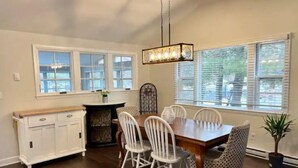 A dining area with a wooden table and white chairs, a white cabinet, and a hanging light fixture. - Charming Home in Reading with a Large Yard (Reading)