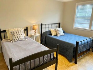 A room with two beds, each with a different style of headboard and bedding. There is a small table with a lamp between the beds.