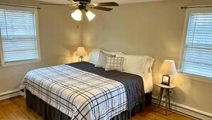 A bedroom with a bed, two bedside lamps, a ceiling fan, and two windows with blinds. - Charming Home in Reading with a Large Yard (Reading)