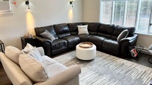 A living room with a sectional sofa, a smaller sofa, a coffee table, and a rug. There are wall-mounted lamps and a window with blinds. - Charming Home in Reading with a Large Yard (Reading)