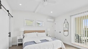 A modern hotel room with a large bed, a ceiling fan, two windows, a bedside table, and a view of the outdoors. - Townhouse in Downtown Gloucester #2 (Gloucester)