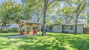 Un patio trasero residencial con una estructura de juego de madera, una casa y un césped bien cuidado.