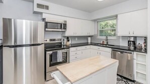 Una cocina moderna con electrodomésticos de acero inoxidable, muebles blancos y suelo con estampado blanco y negro.