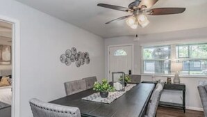 Comedor con una mesa de madera oscura, sillas tapizadas en gris, un ventilador de techo y un elemento decorativo en la pared.