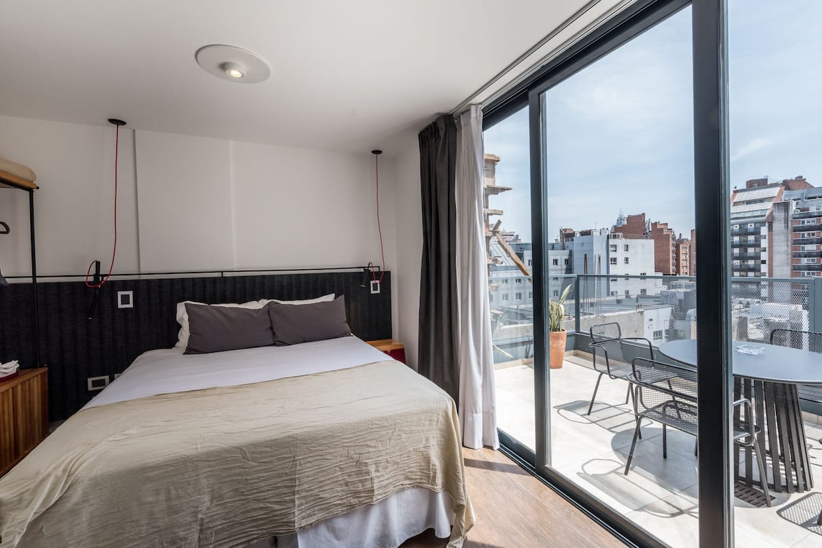 Une chambre d’hôtel moderne dotée d’un grand lit, d’un balcon avec une table et des chaises, et offrant une vue sur la ville.