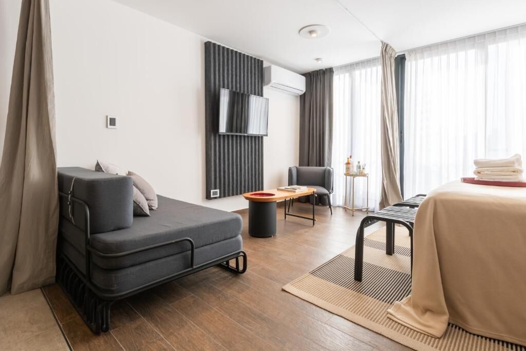Ein modernes Hotelzimmer mit Sofa, kleinem Tisch, Bett und einem an der Wand befestigten Fernseher.