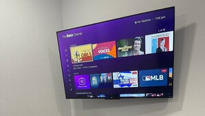 Een flatscreen televisie aan een muur met een streamingdienst interface, verschillende kanalen en programma’s.