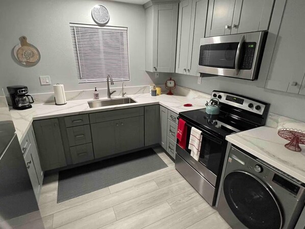 A modern kitchen with grey cabinets, a stainless steel sink, a microwave, an oven, and a washing machine.